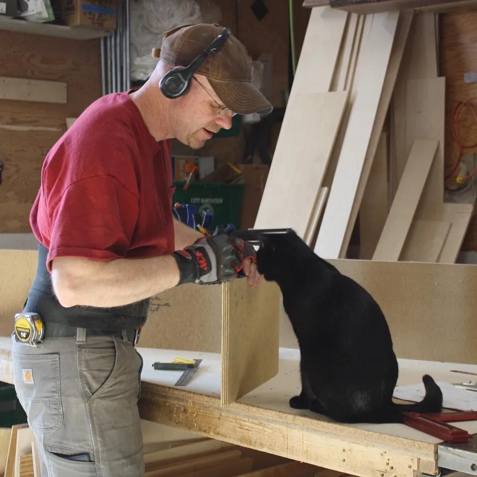 A maker at work in a Northside studio workshop, with a cat watching from the bench.